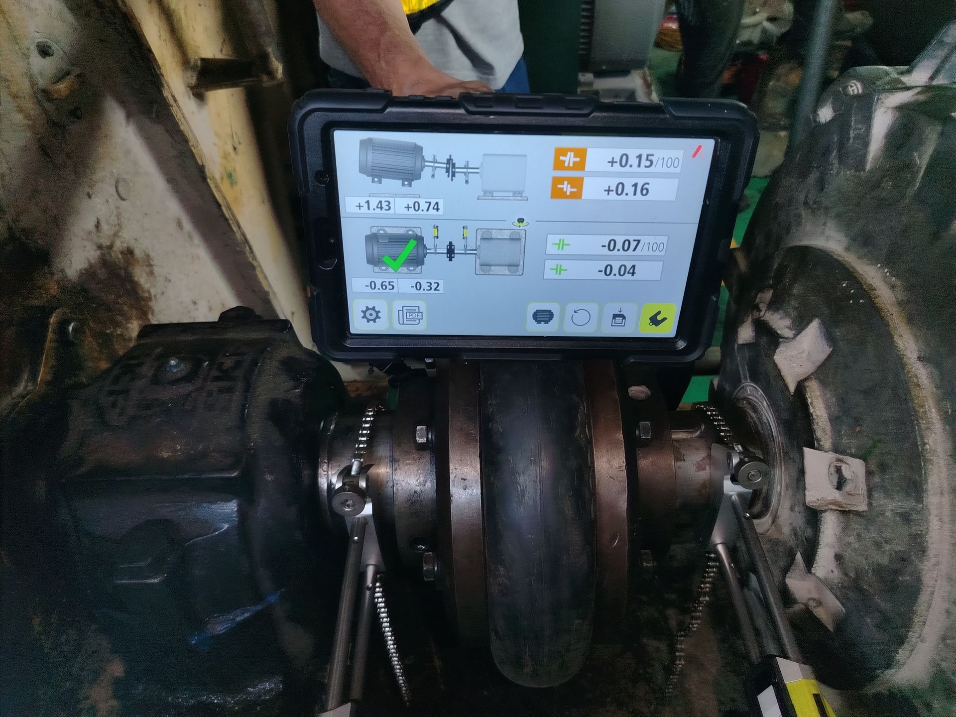 Persona que utiliza una tableta para medir la alineación de las ruedas del tractor, con herramientas visibles.