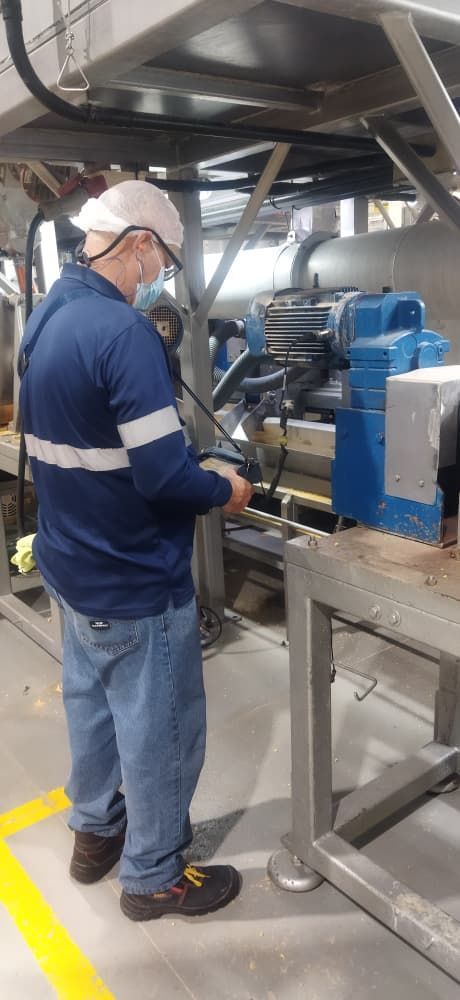 Una persona que usa casco, máscara y camisa de trabajo azul opera maquinaria en una fábrica.