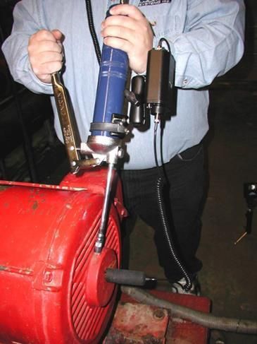 Una persona usa una herramienta en un motor rojo. La herramienta es azul y está conectada a una caja negra.