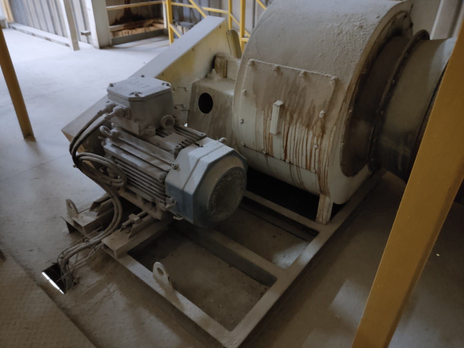 Motor y maquinaria industrial, cubiertos de polvo, montados sobre un marco metálico, en un entorno fabril.