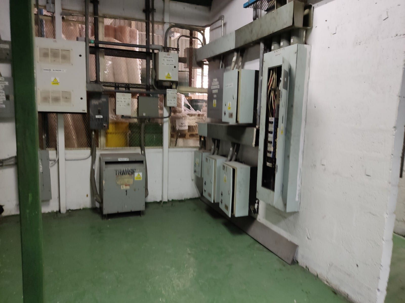 Sala de paneles eléctricos con varias cajas grises, tuberías y piso verde.