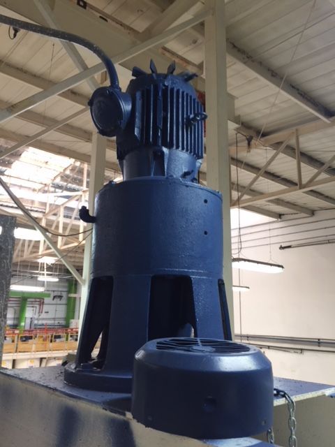 Maquinaria industrial azul, probablemente un motor, encima de una plataforma en un entorno de fábrica.