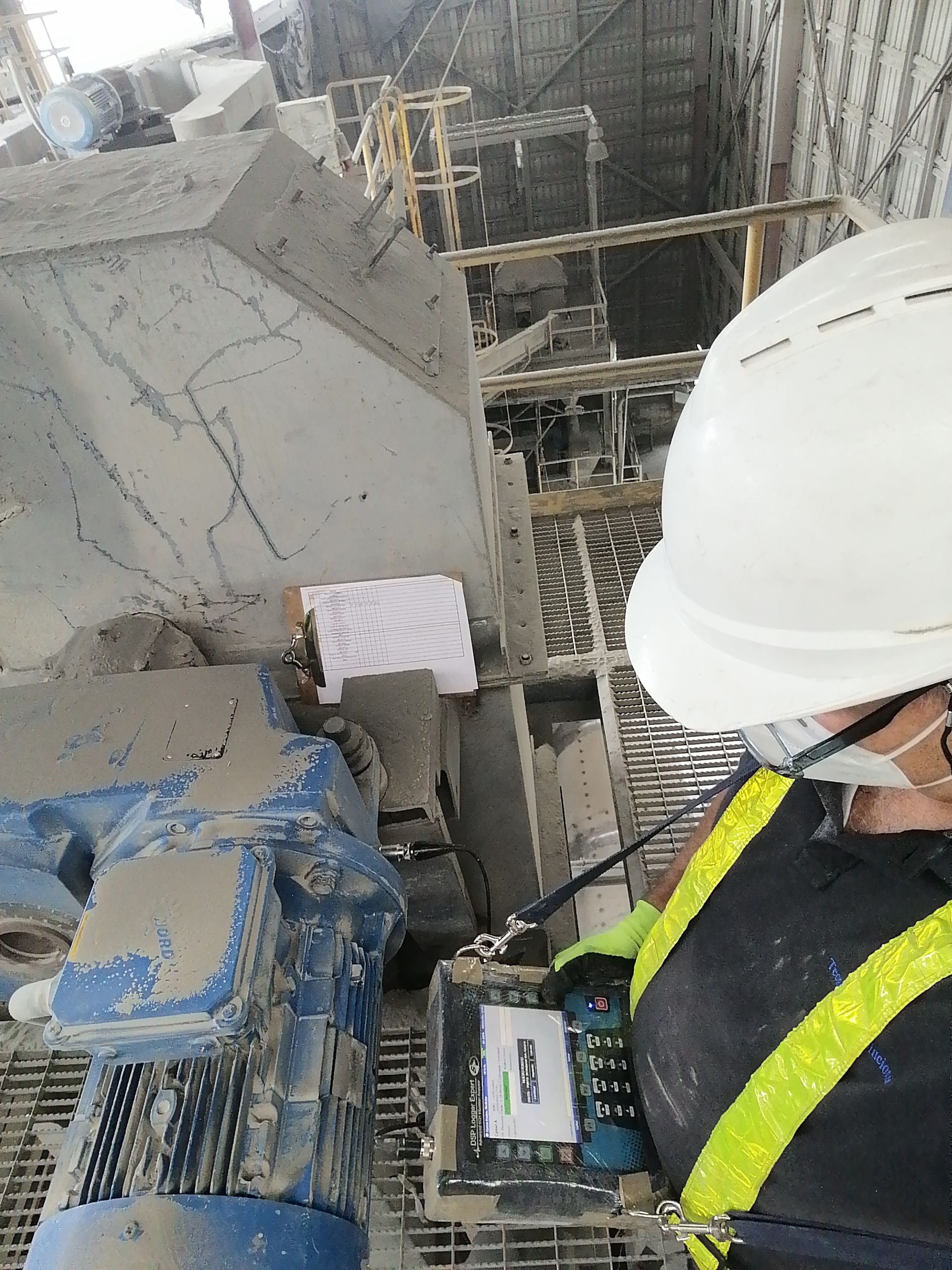 Trabajador con casco operando maquinaria en una fábrica, sosteniendo un panel de control.