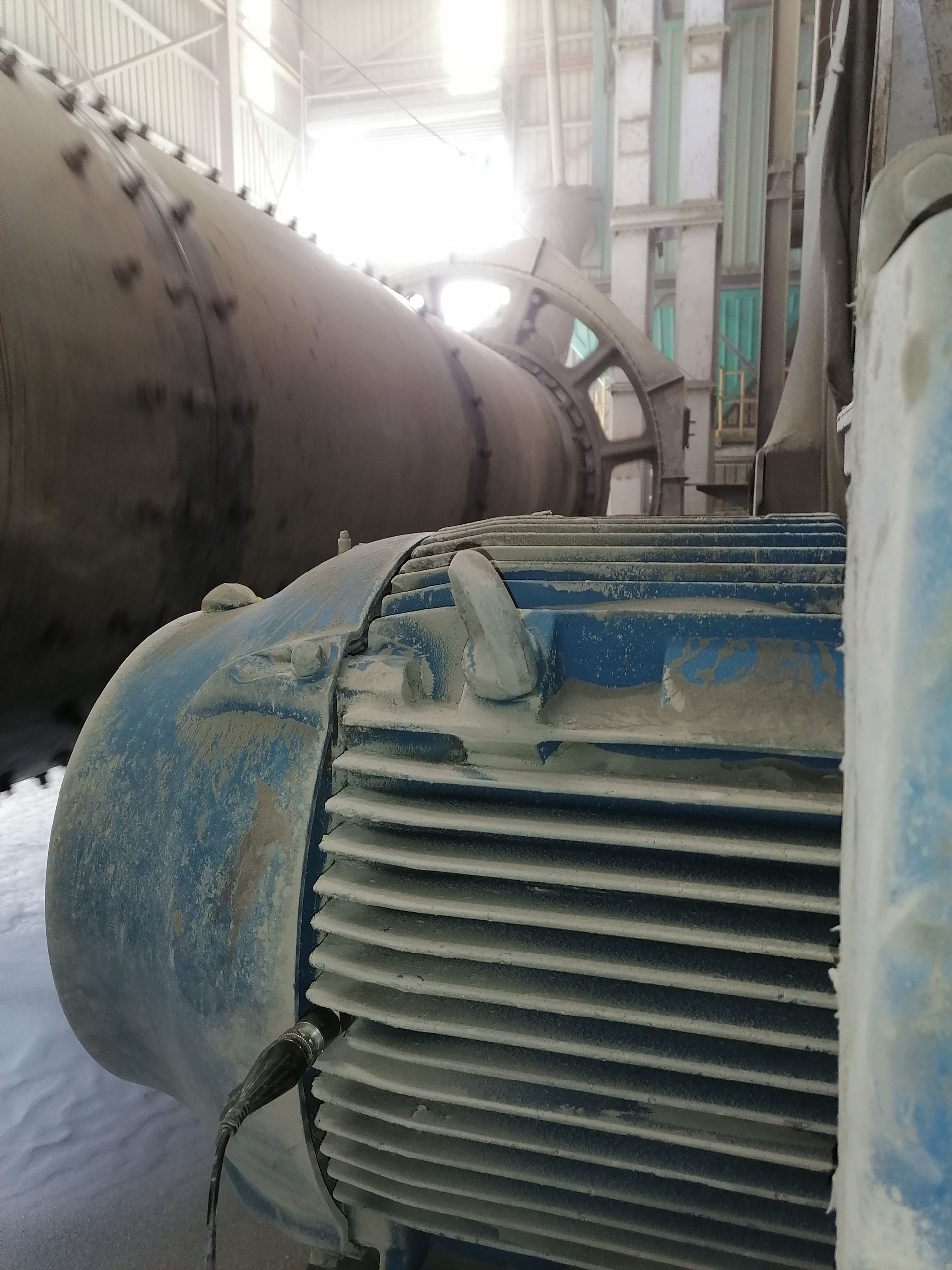 Gran motor eléctrico azul con aletas en un entorno industrial, junto a una máquina cilíndrica.