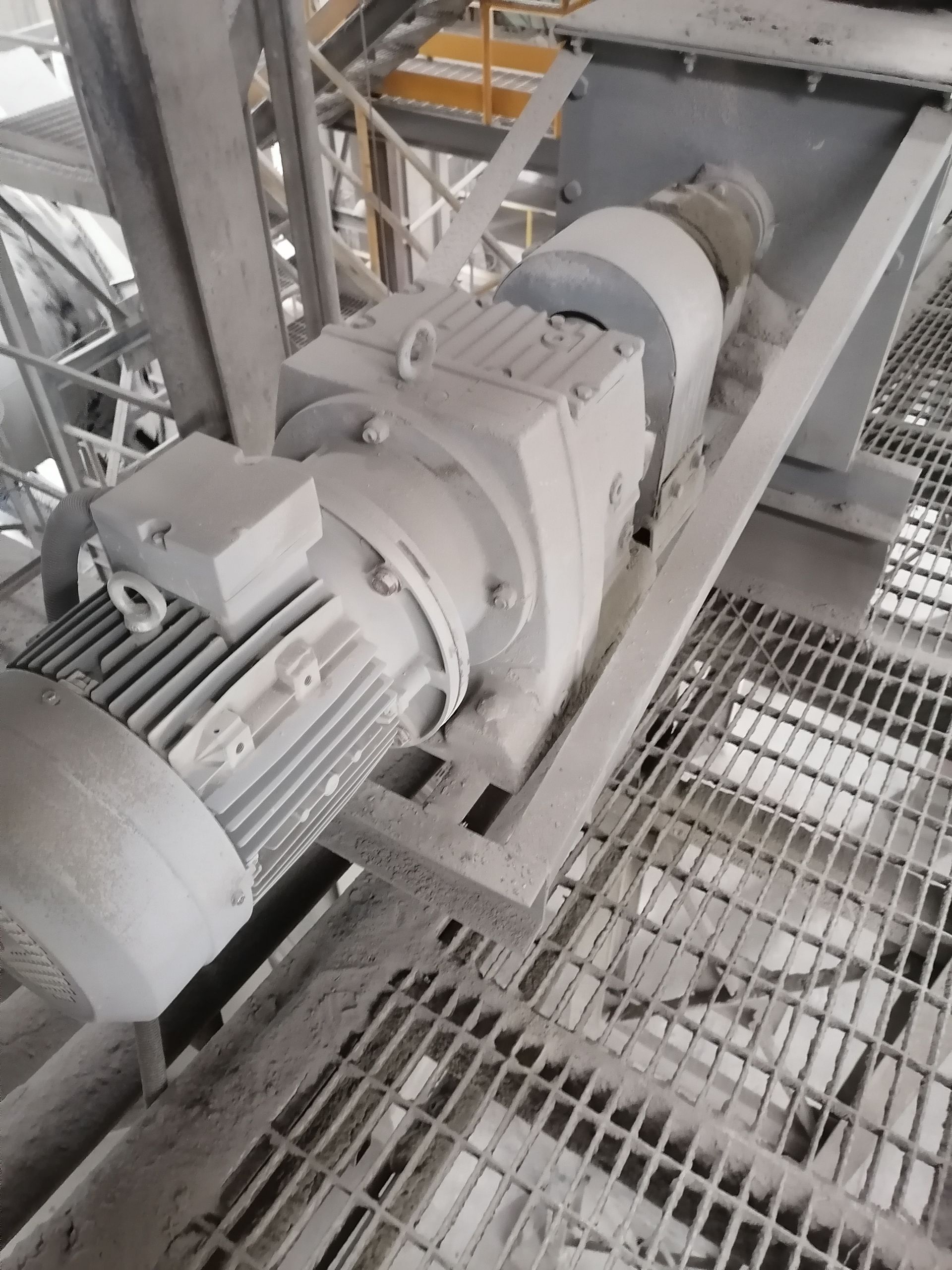 Motor eléctrico y caja de cambios sobre plataforma metálica en entorno industrial.