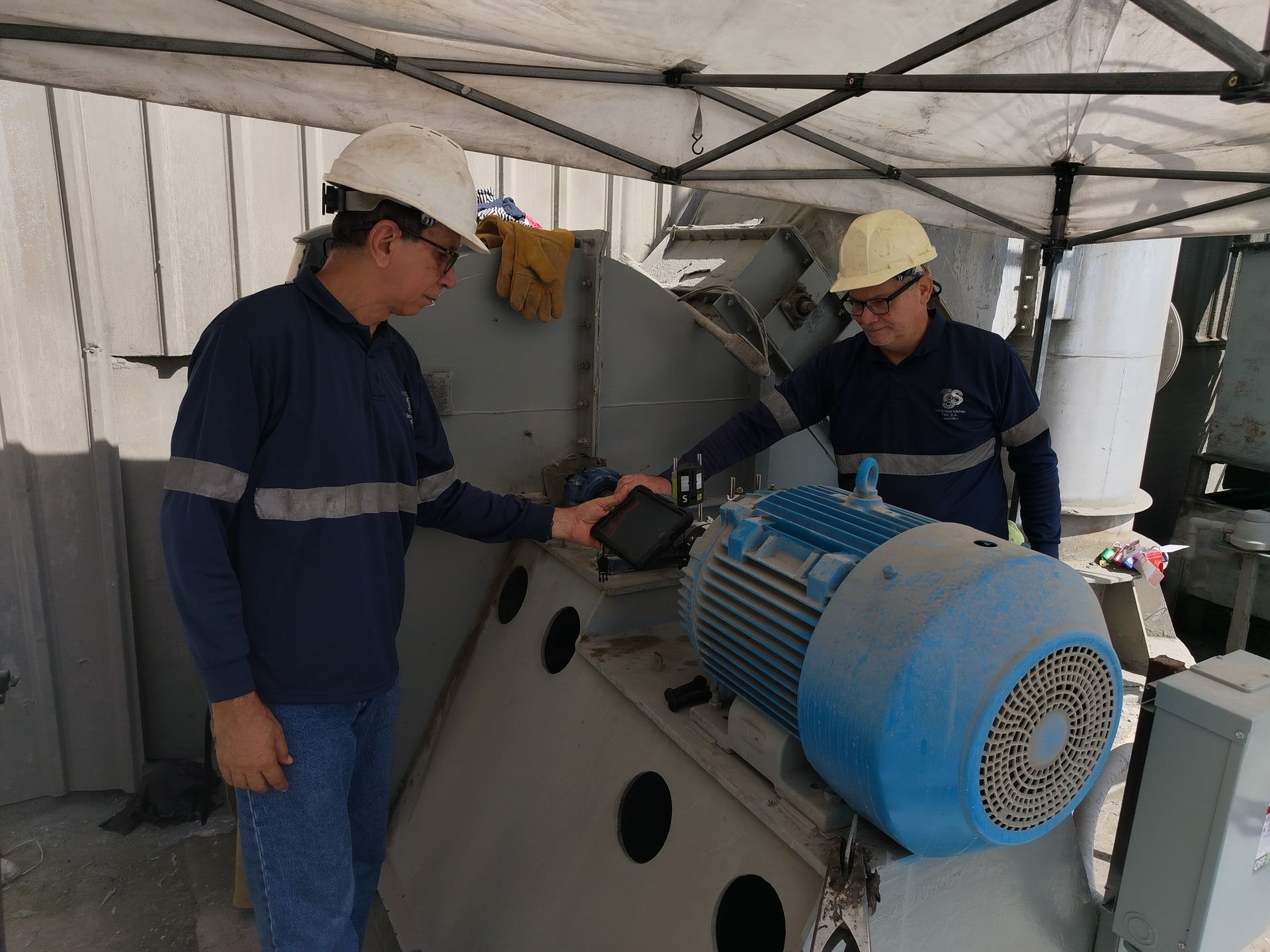 Dos trabajadores con cascos inspeccionando un gran motor azul; entorno industrial.
