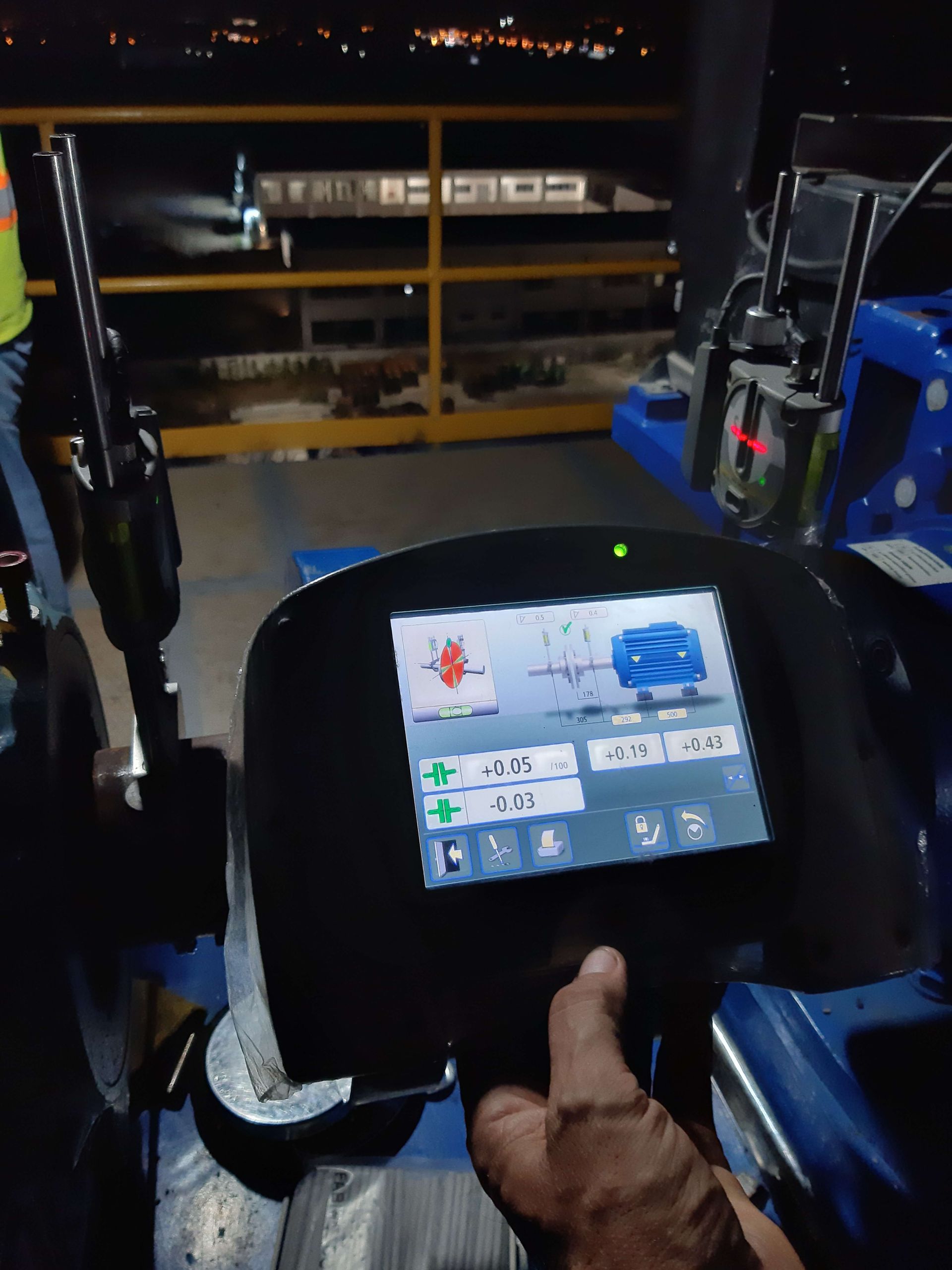 Una persona utiliza el panel de control de una máquina azul por la noche. La pantalla muestra las lecturas de alineación.