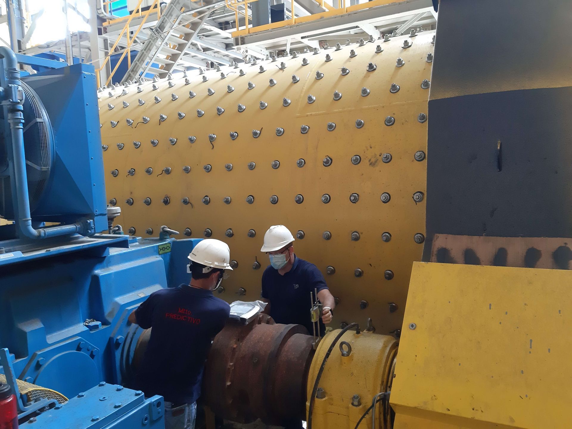 Dos trabajadores con cascos inspeccionan una gran máquina industrial amarilla.