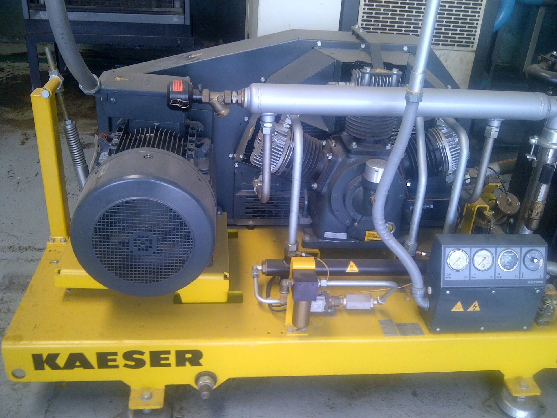 Máquina compresora de aire Kaeser de color amarillo con motor gris y tuberías de metal.
