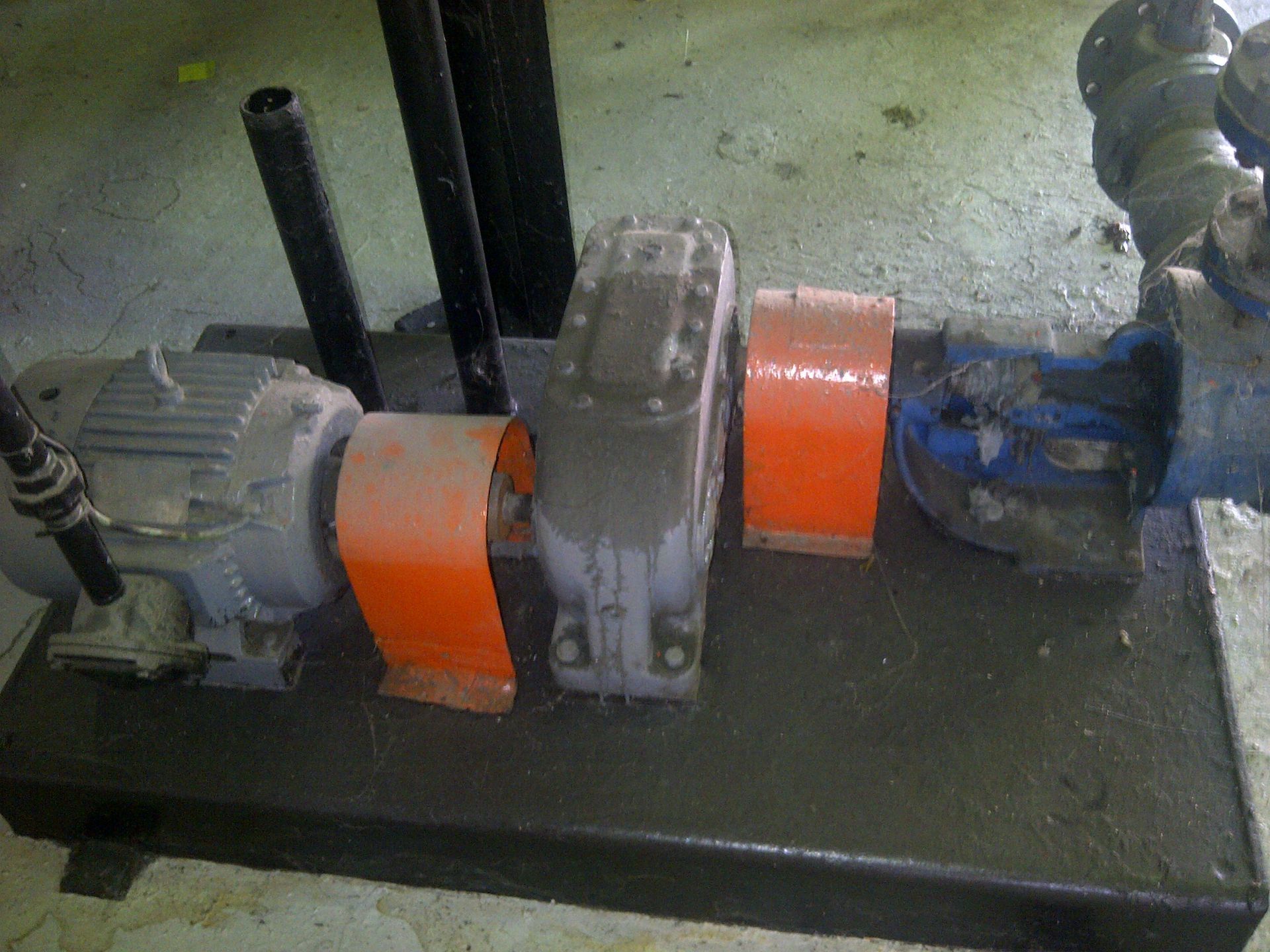 Conjunto de motor eléctrico, caja de cambios y bomba sobre base metálica, con tapas de seguridad de color naranja.