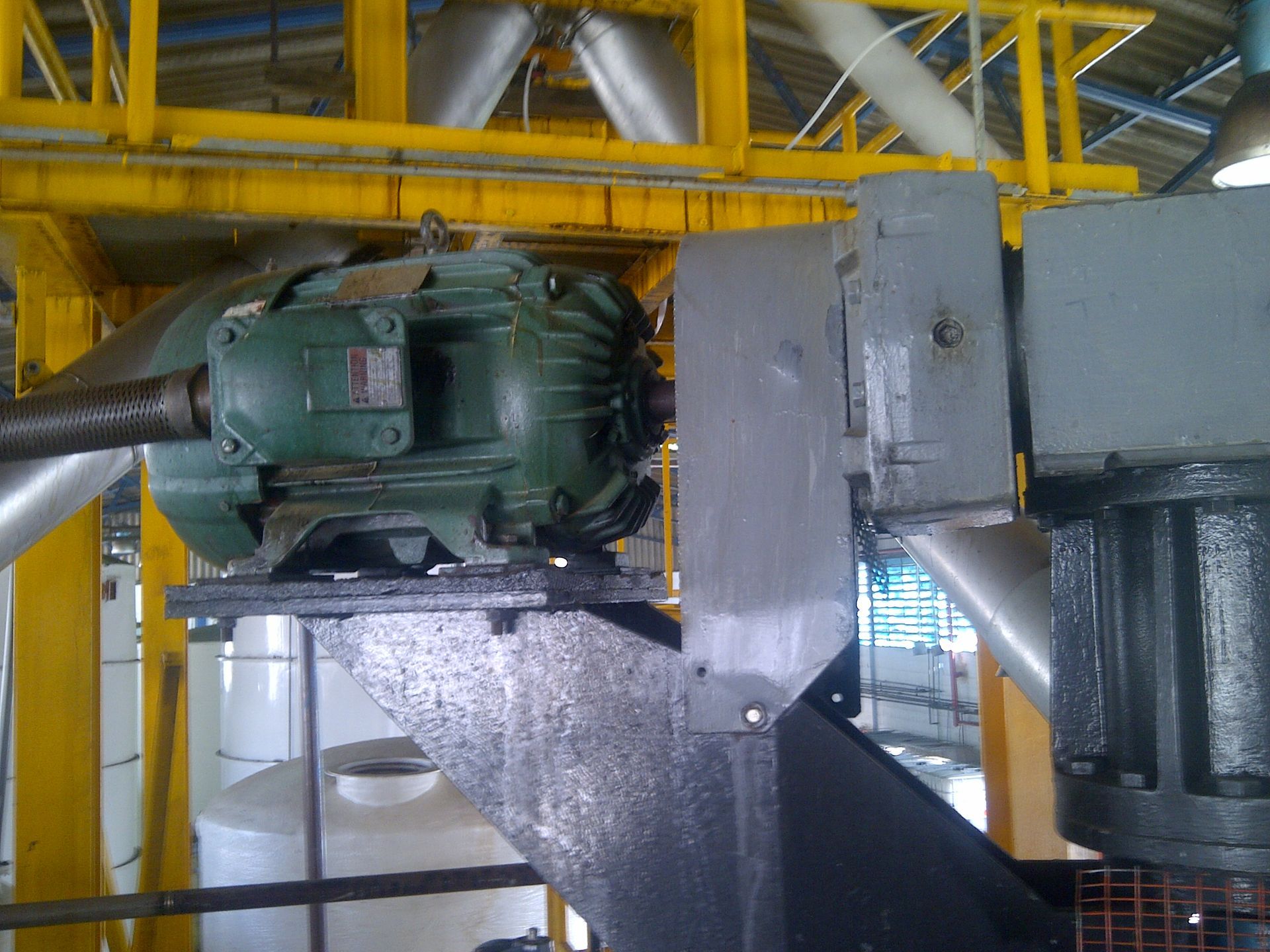 Motor industrial verde sobre plataforma metálica, estructura de soporte amarilla, ambientación interior.