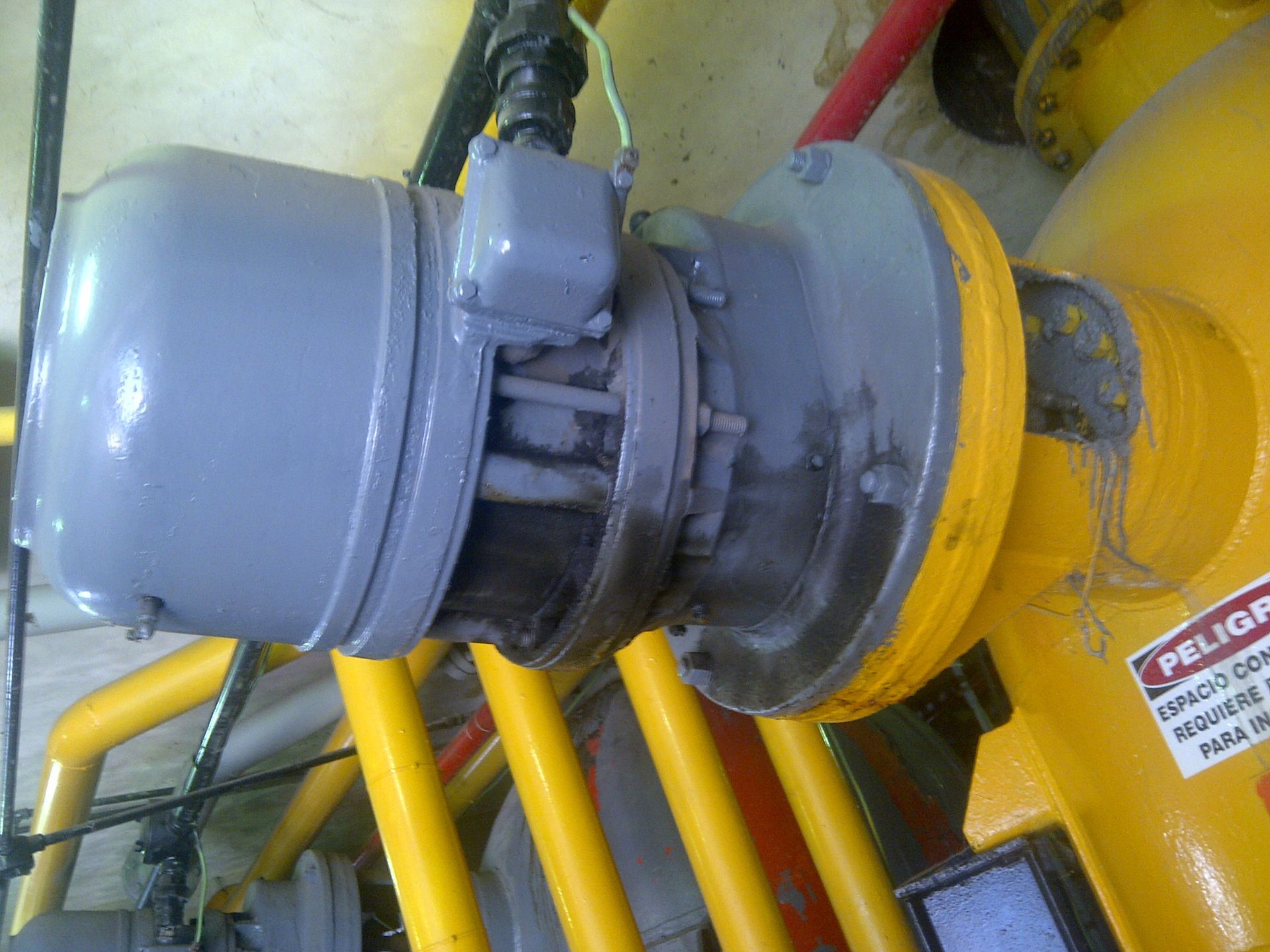 Motor pintado de gris unido a una máquina industrial amarilla, con tuberías visibles.