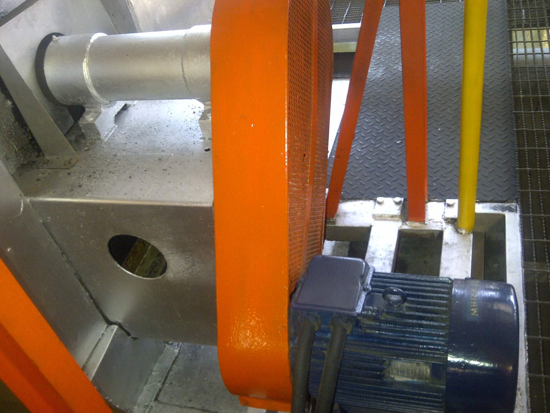 Transmisión por correa de color naranja conectada a un motor eléctrico de color azul, con maquinaria metálica.