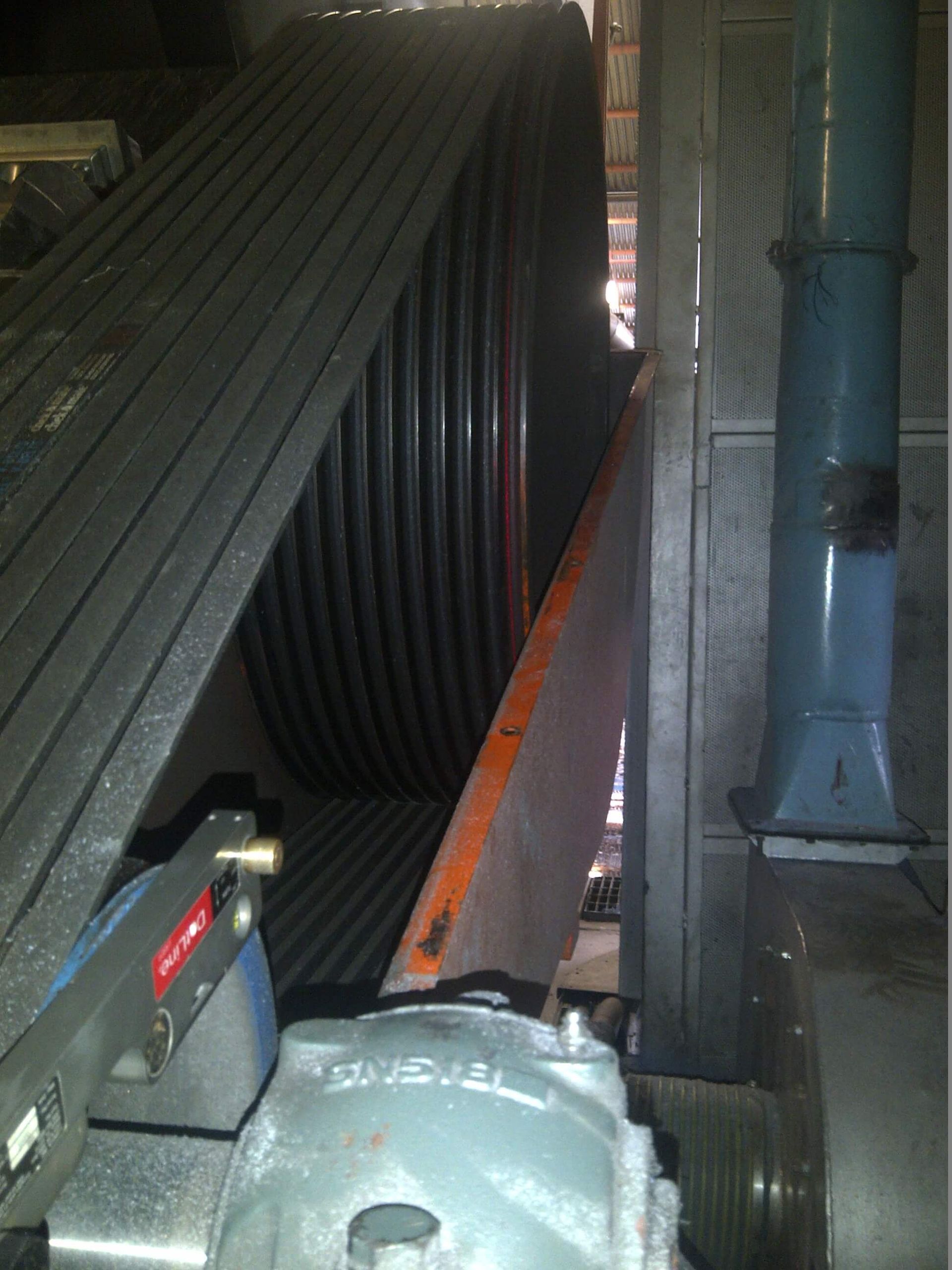 Sistema de correa y polea industrial de gran tamaño con estructura gris y naranja.