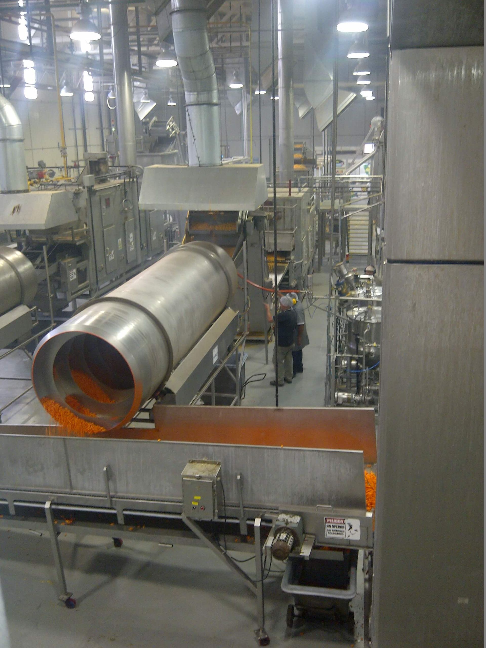 Gran máquina industrial que dispensa producto alimenticio de color naranja sobre una cinta transportadora.