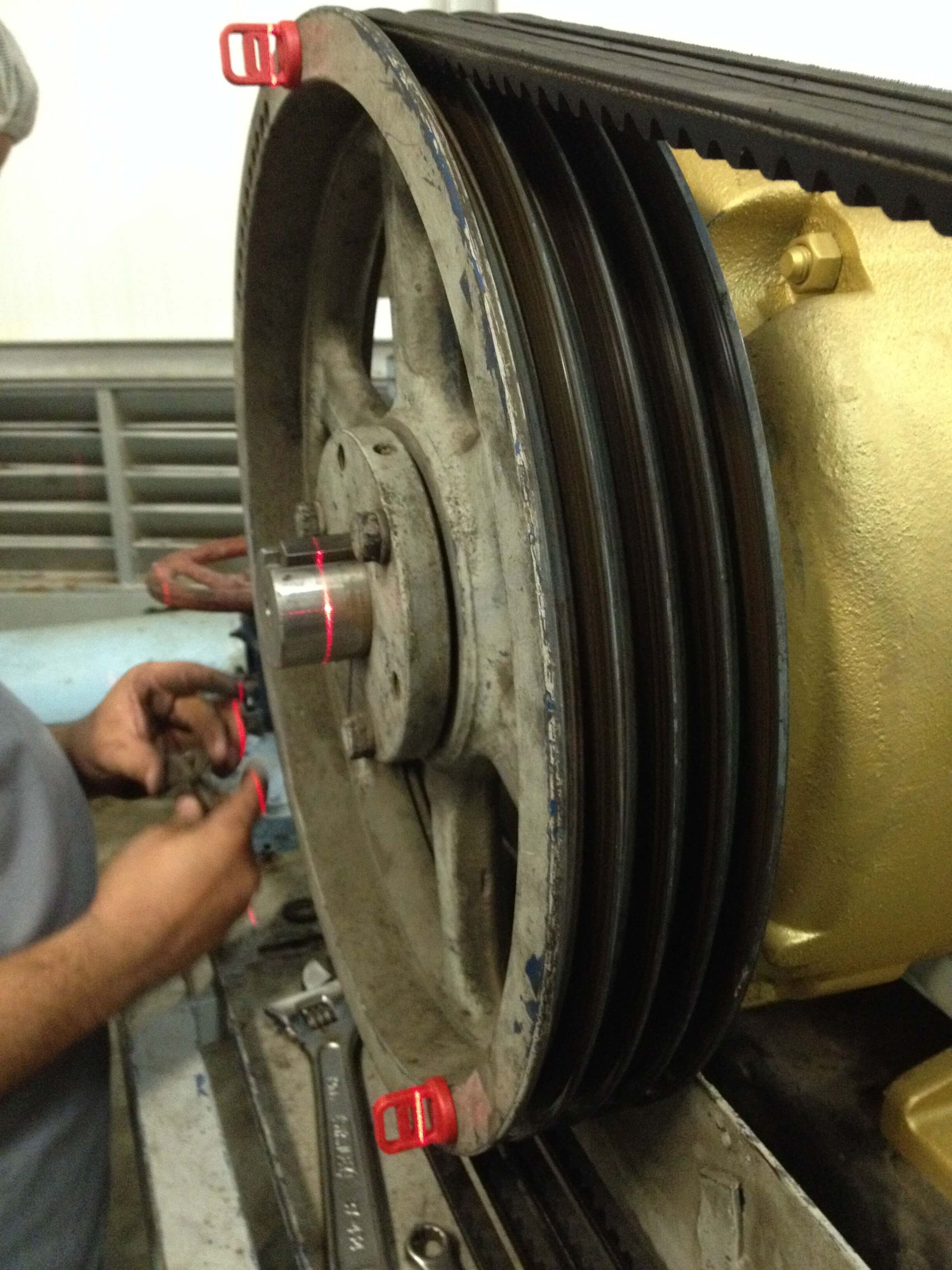 Un mecánico alinea una polea grande con herramientas láser en un equipo industrial; láseres rojos visibles.