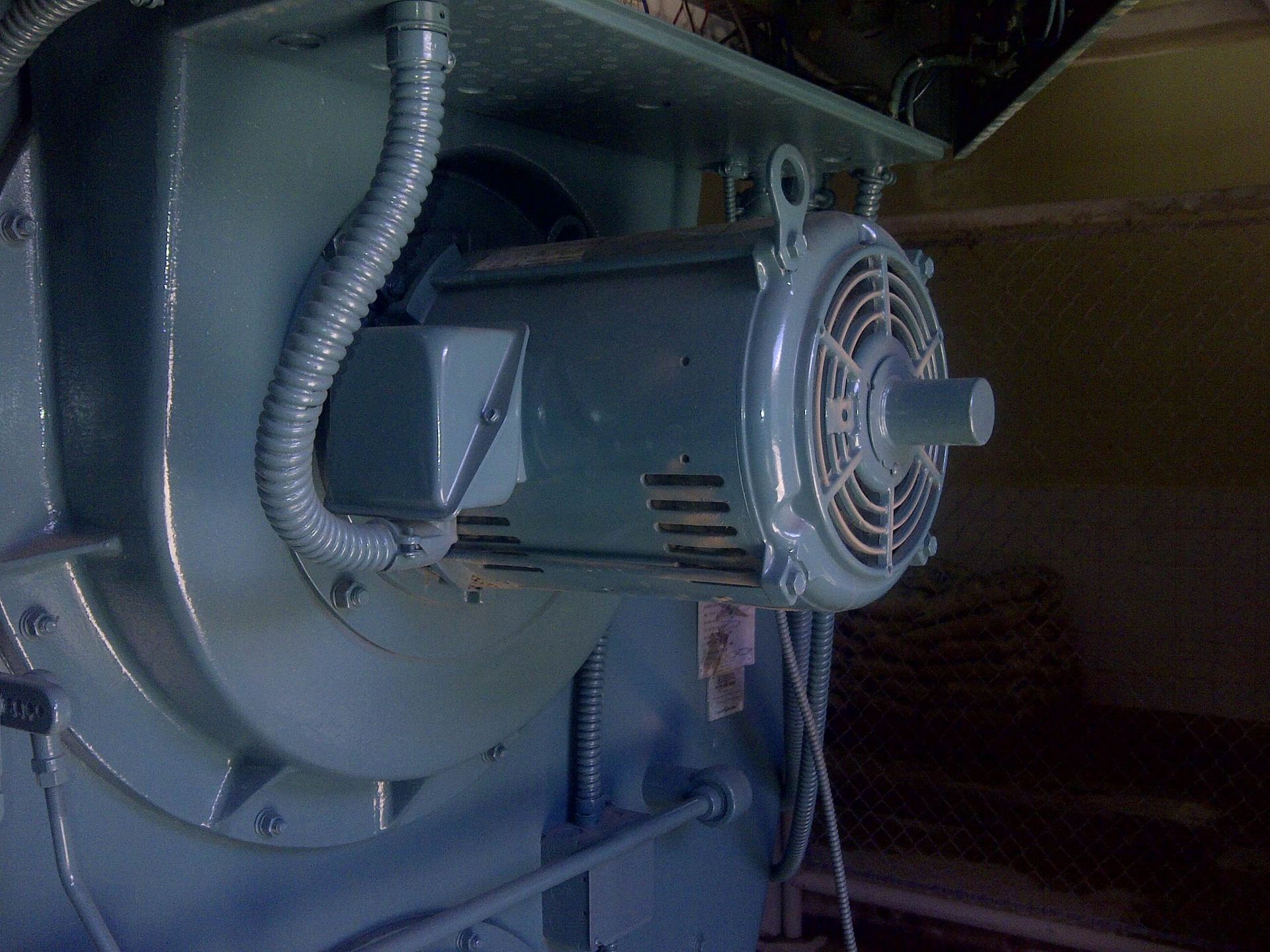 Un motor eléctrico industrial grande, de color verde azulado, con un ventilador acoplado, montado en una máquina.