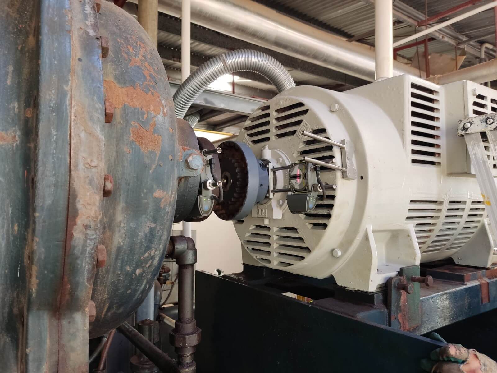 Un gran generador eléctrico acoplado a un componente industrial azul oxidado; situado en una fábrica.