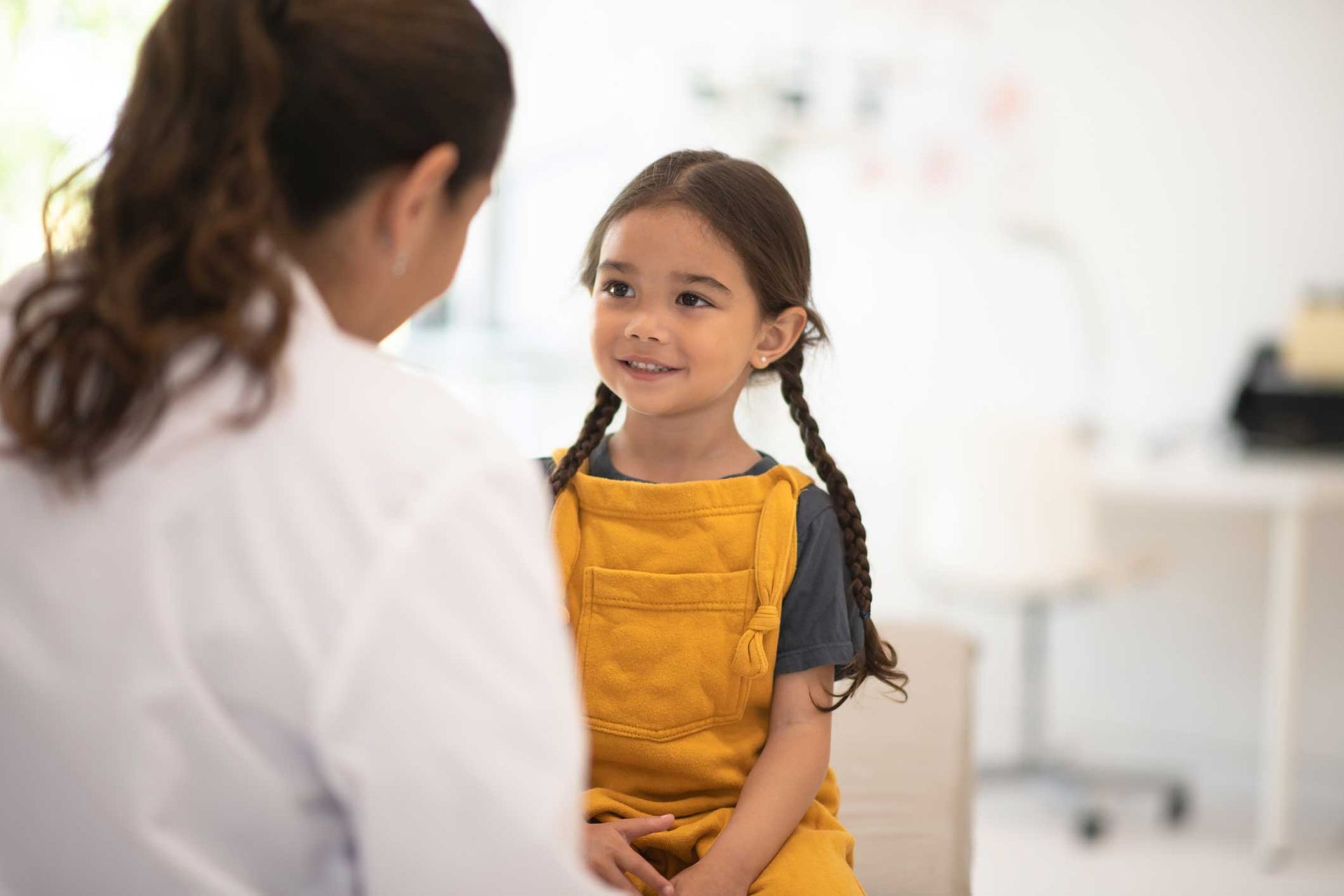 A little girl is sitting on a couch talking to a doctor.