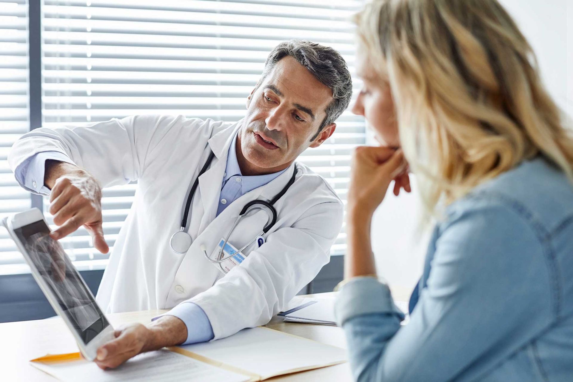 A doctor is talking to a patient while looking at an x-ray on a tablet.