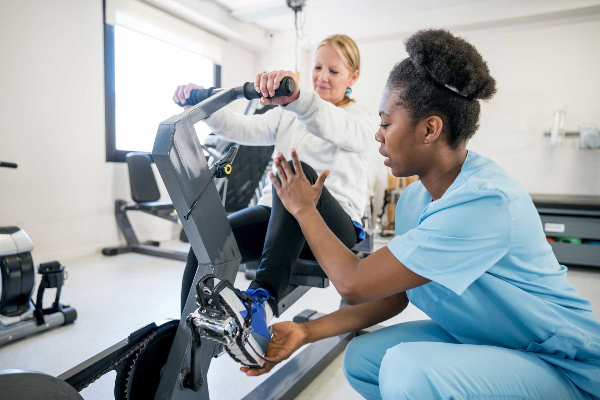 A nurse is helping a woman on an exercise bike.