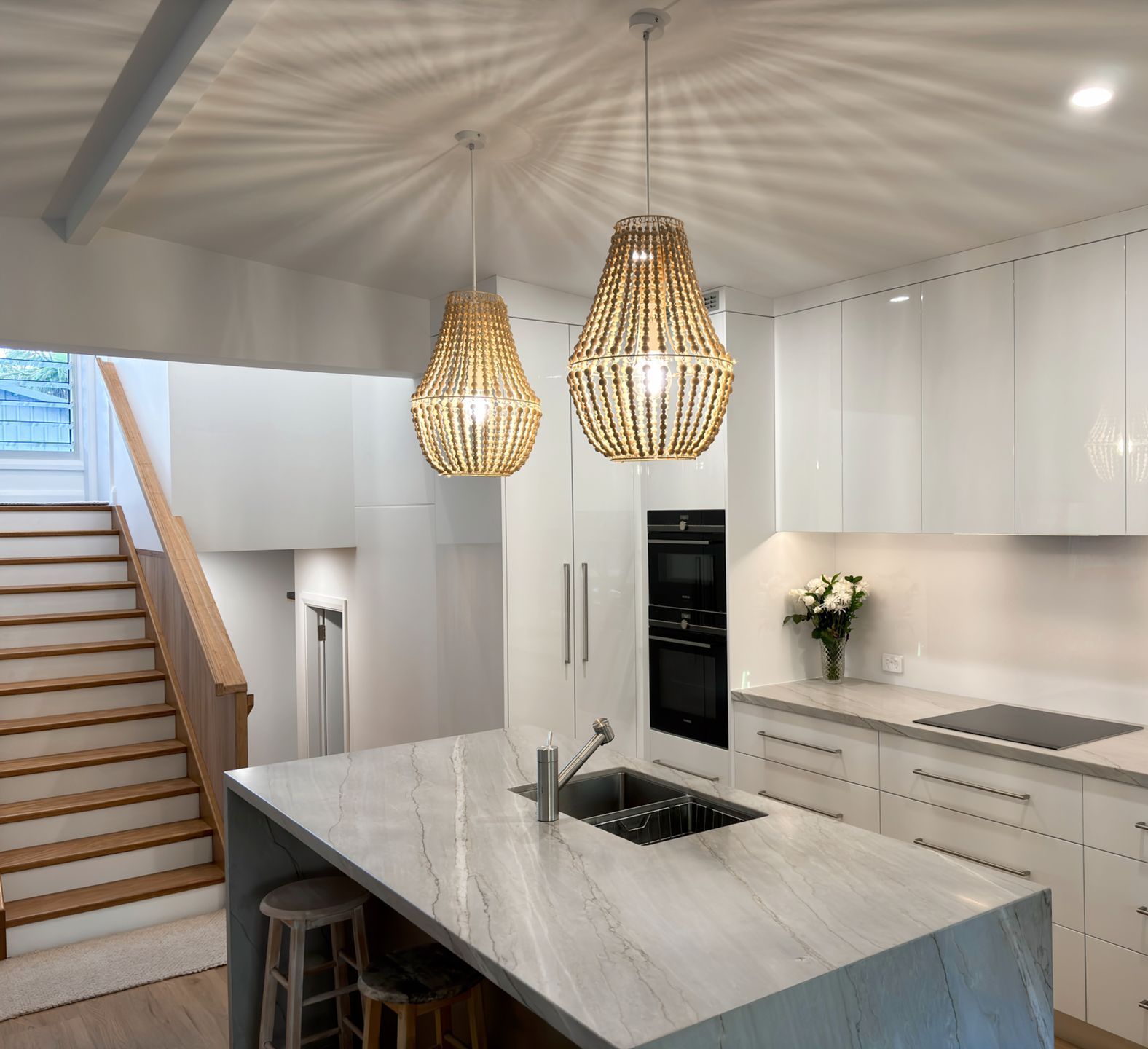 A kitchen with white cabinets and a large island in the middle with feature lighting above. 