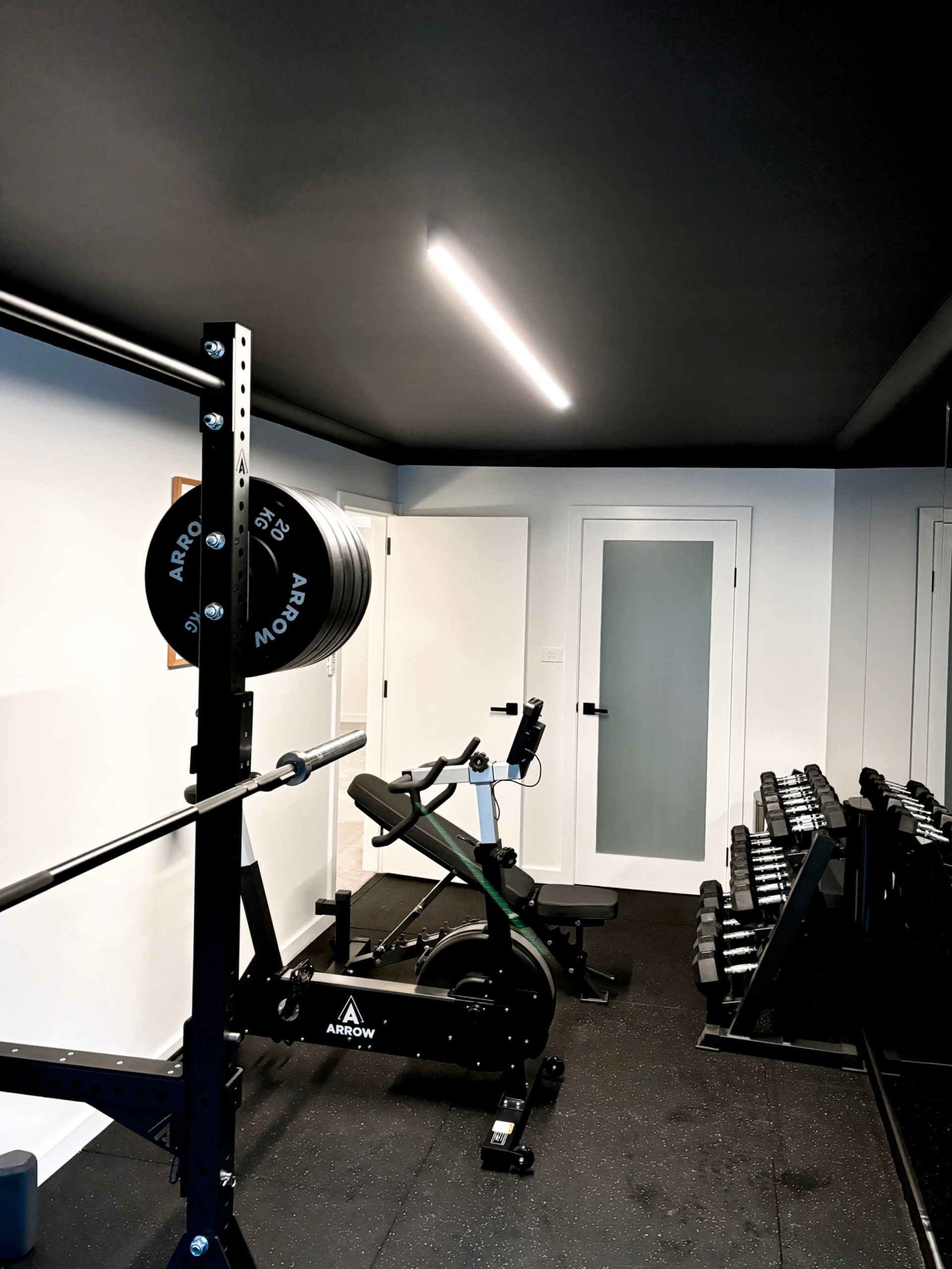 A gym with a row of dumbbells and a squat rack with LED strip lighting. 