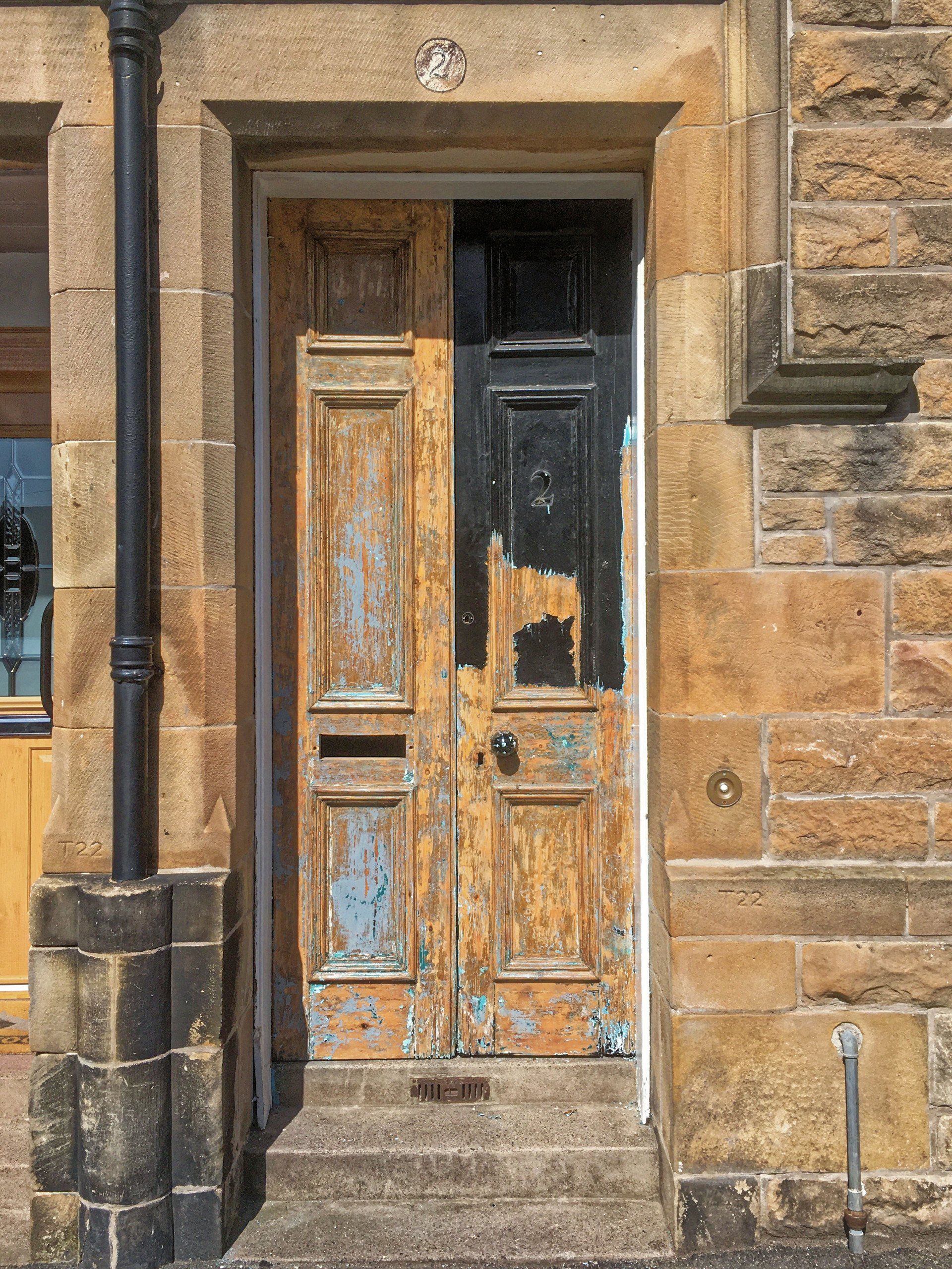 An old wooden door with peeling paint is on a stone building.
