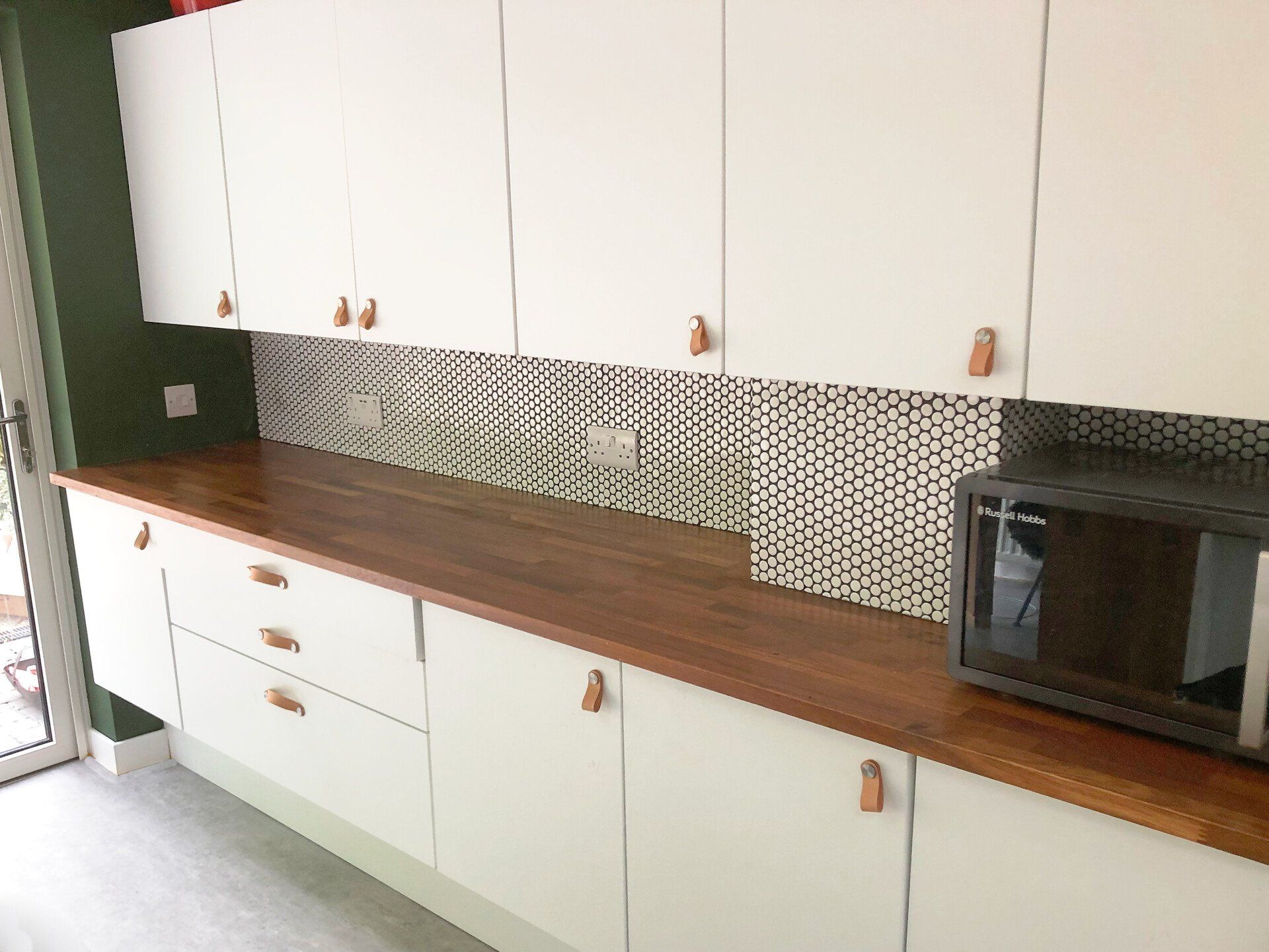 A kitchen with white cabinets , wooden counter tops , and a microwave.