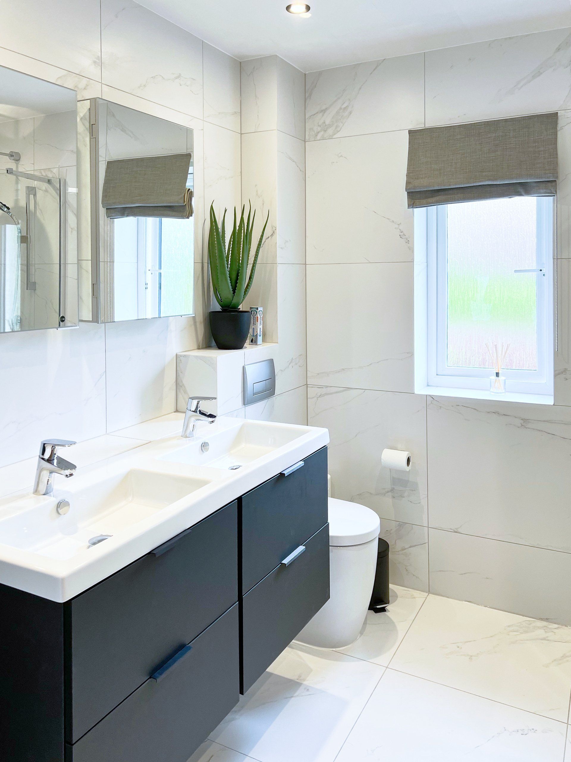 A bathroom with a sink , toilet , mirror and window.