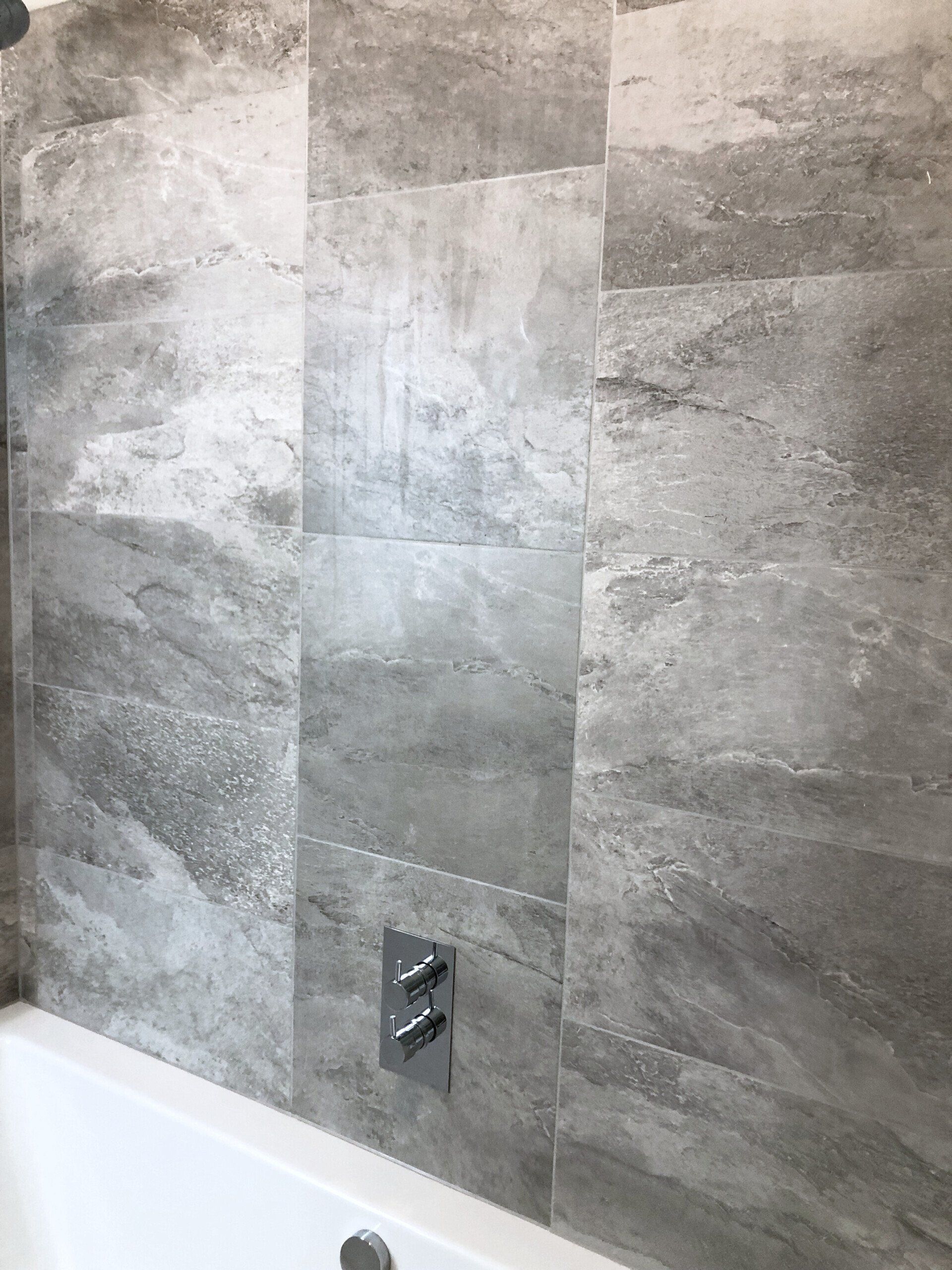A bathroom with gray tiles on the wall and a bathtub.