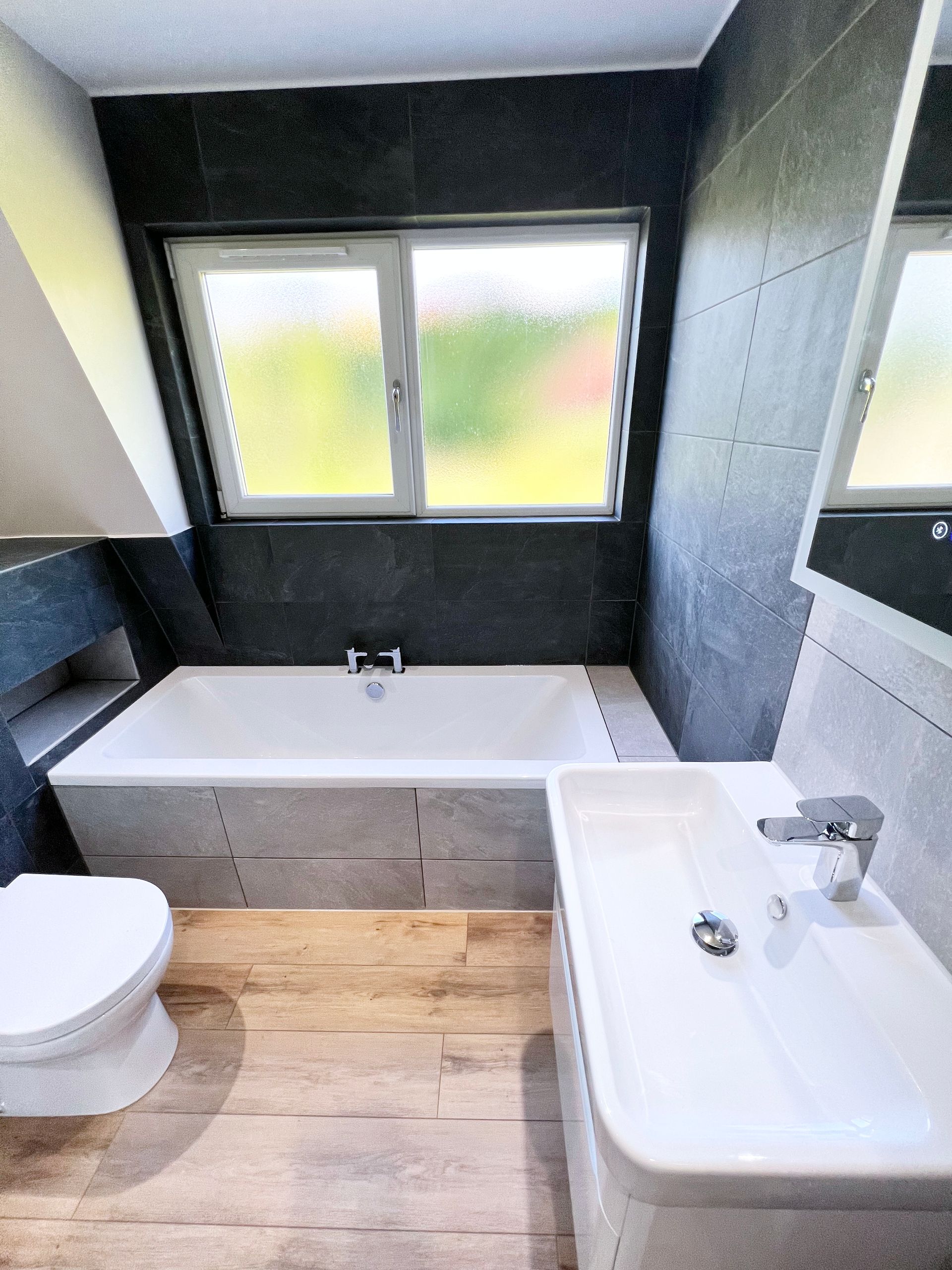 A bathroom with a toilet , sink , bathtub and window.