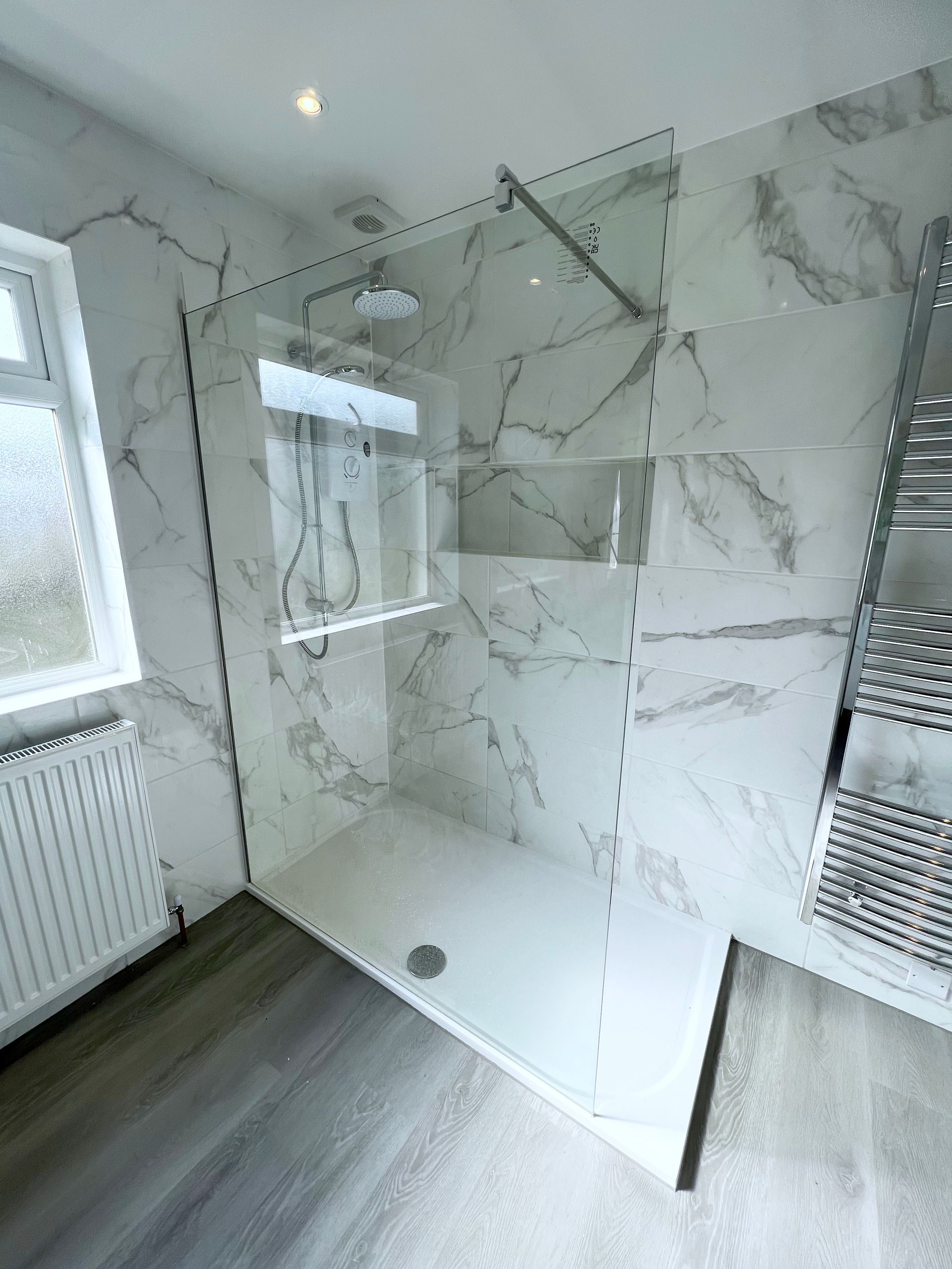A bathroom with a walk in shower and marble tiles on the walls.