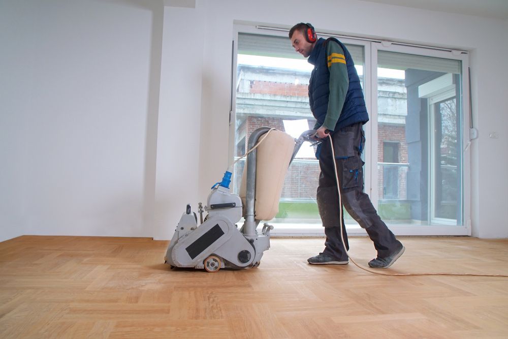 A Man Is Sanding A Wooden Floor With A Machine — Byron Floor Sanding In Lismore, NSW