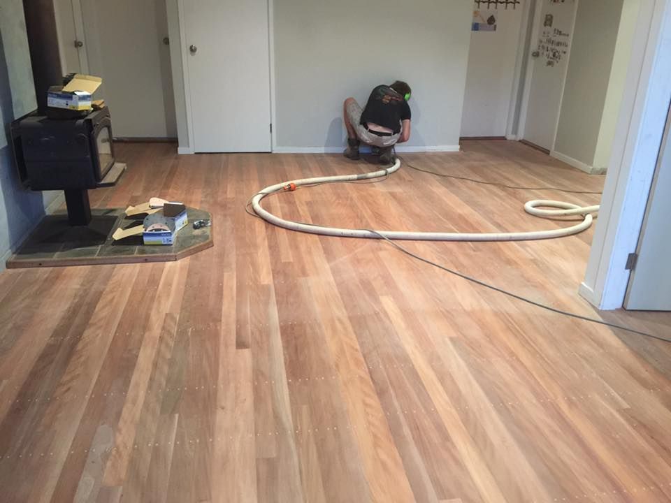 A Man Is Kneeling On A Wooden Floor In A Living Room — Byron Floor Sanding In Tintenbar, NSW