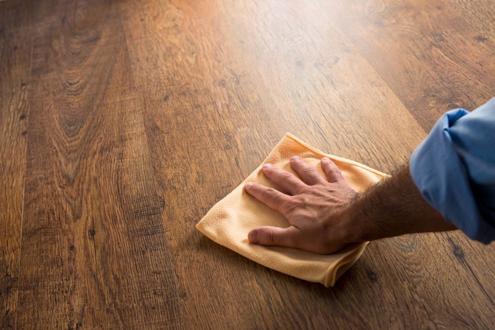 A Person Is Cleaning A Wooden Floor With A Cloth — Byron Floor Sanding In Lismore, NSW