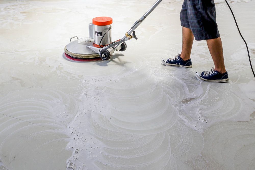 A Man Is Cleaning A Concrete Floor With A Machine — Byron Floor Sanding In Yamba, NSW