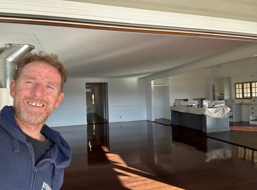 A Man In A Room Smiling at Camera With Wooden Floor In the Background — Byron Floor Sanding In Tintenbar, NSW