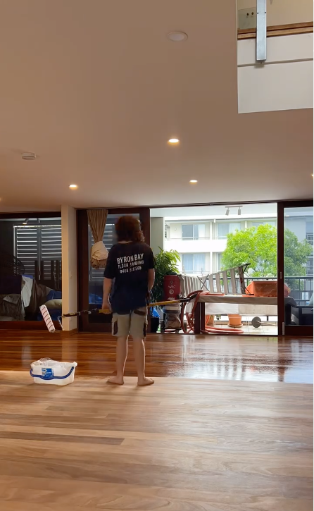 A Man Standing With A Mop and Plastic Container Polishing A Wooden Floor — Byron Floor Sanding In Casino, NSW