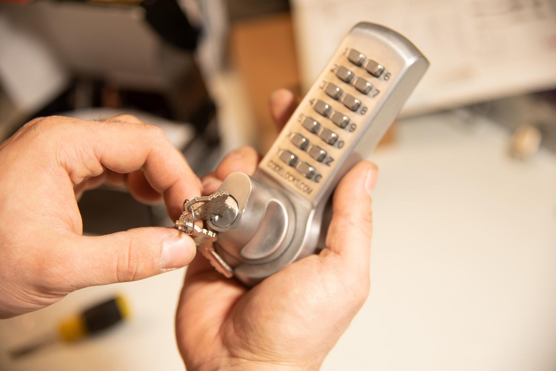 Hands holding a keypad lock with keys; appears to be repair or installation in progress.
