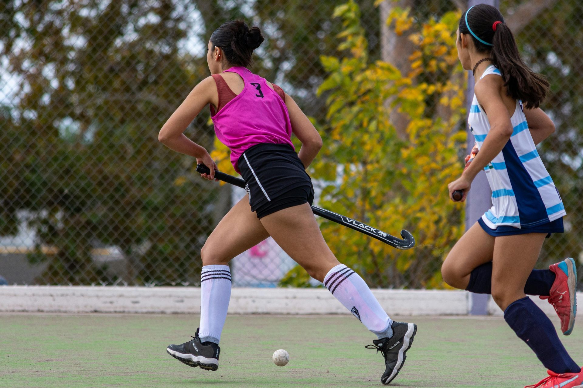 Two girls are playing field hockey on a field.