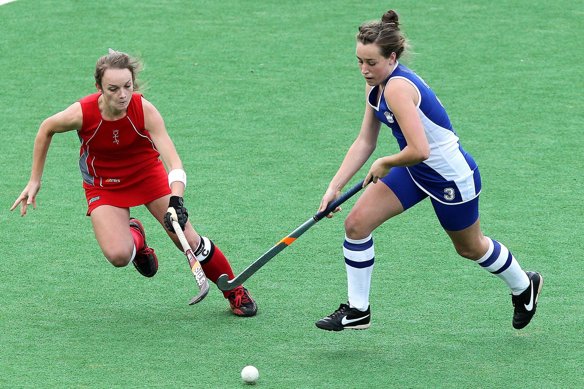 Two women are playing field hockey on a field