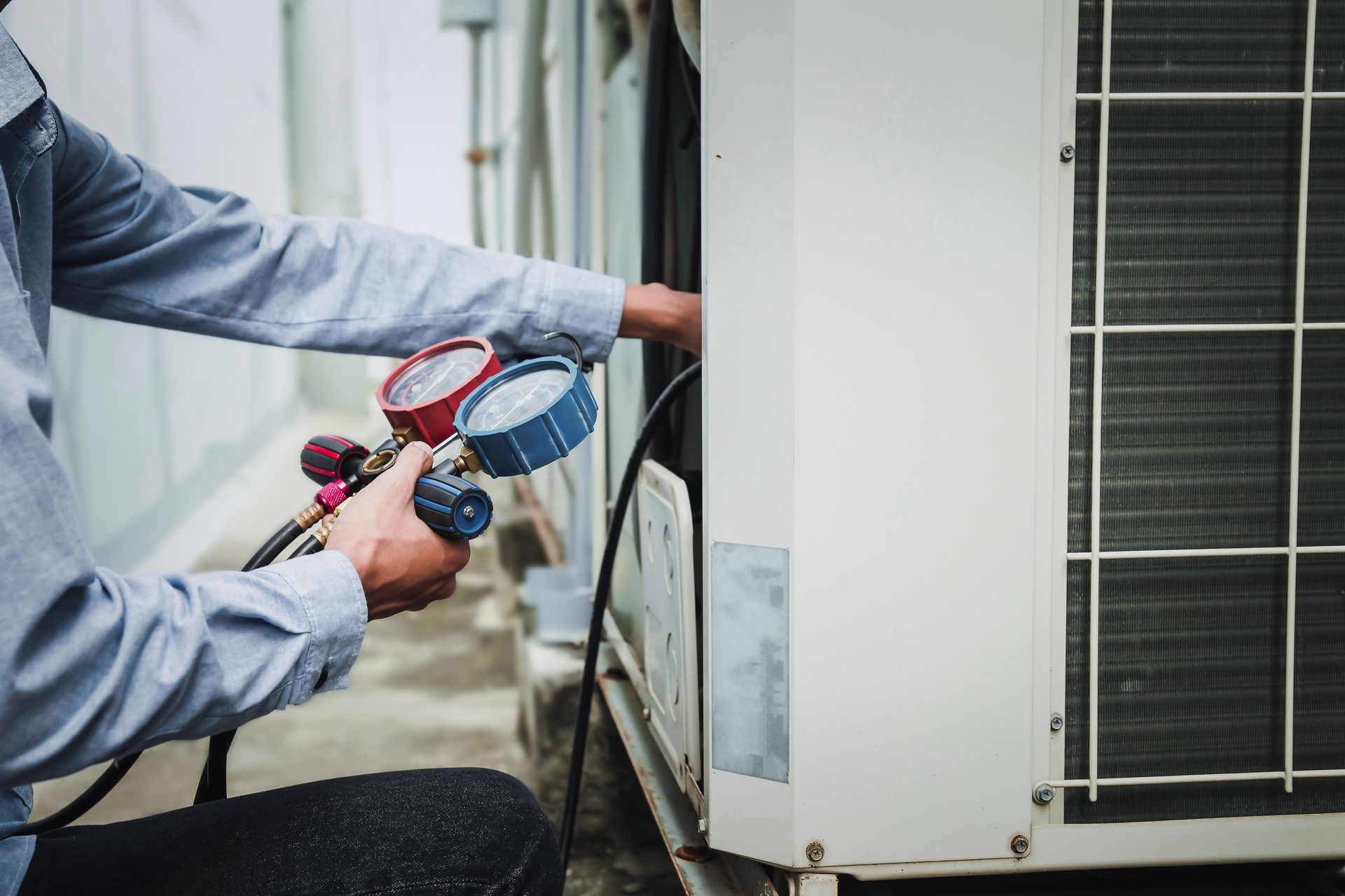 Technician using pressure gauges to diagnose an outdoor air conditioning condenser unit.