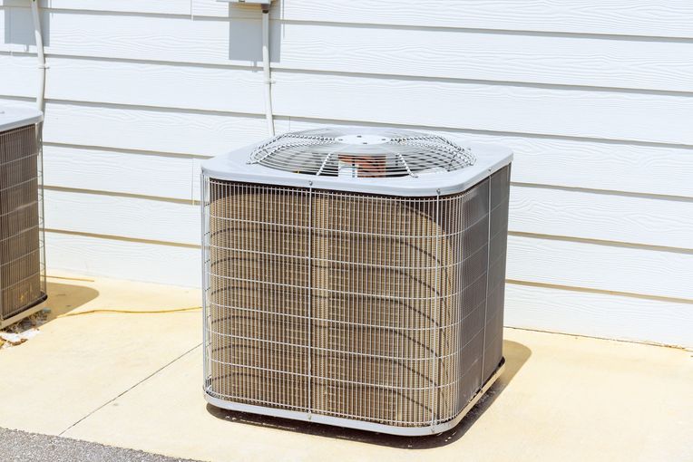 A beige outdoor air conditioning unit sits on a concrete pad against white horizontal siding.