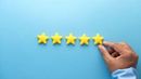 A hand placing a fifth yellow star in a row on a light blue background to complete a five-star rating.