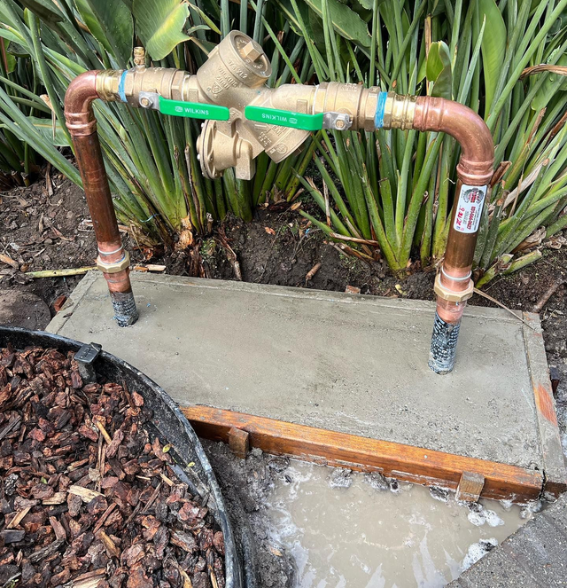 Copper and brass irrigation valve system installed on a concrete base, set in a garden bed.