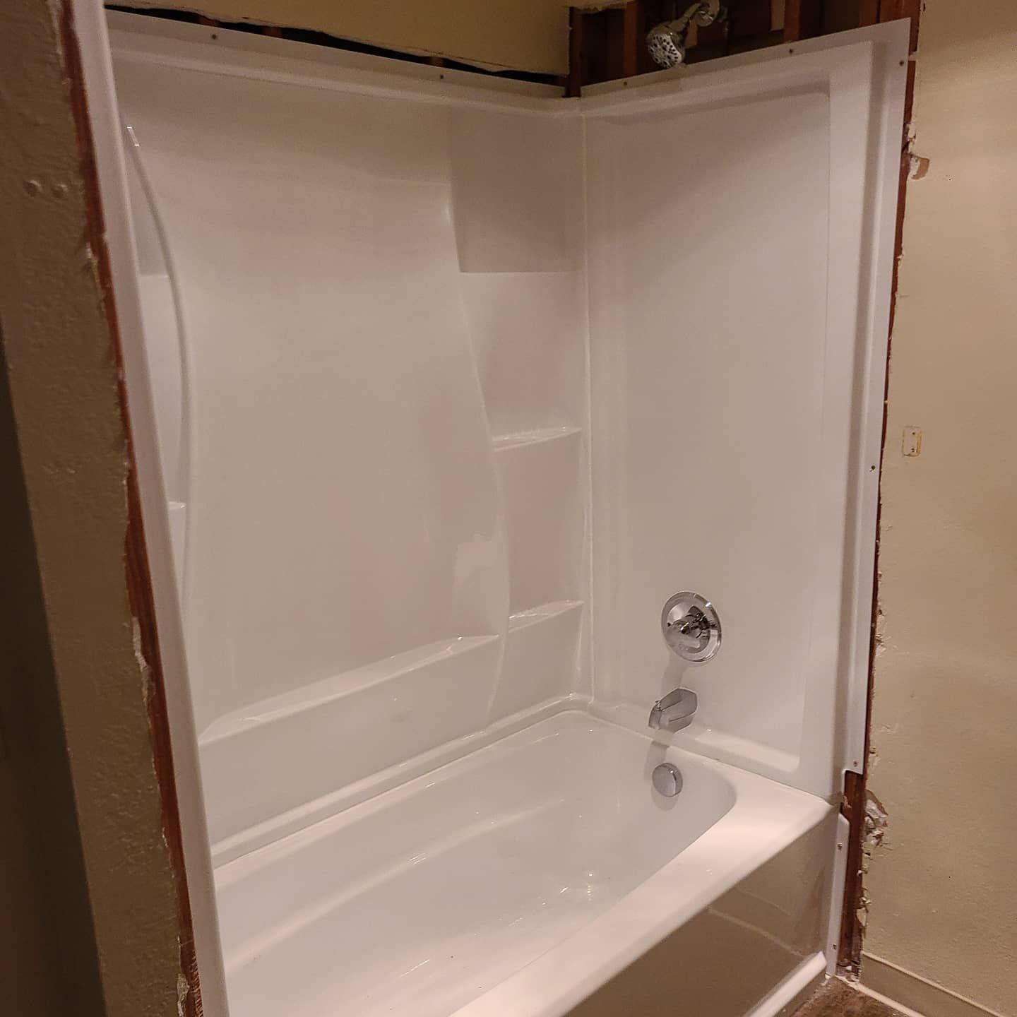 White bathtub and shower surround installed in a bathroom with exposed framing.