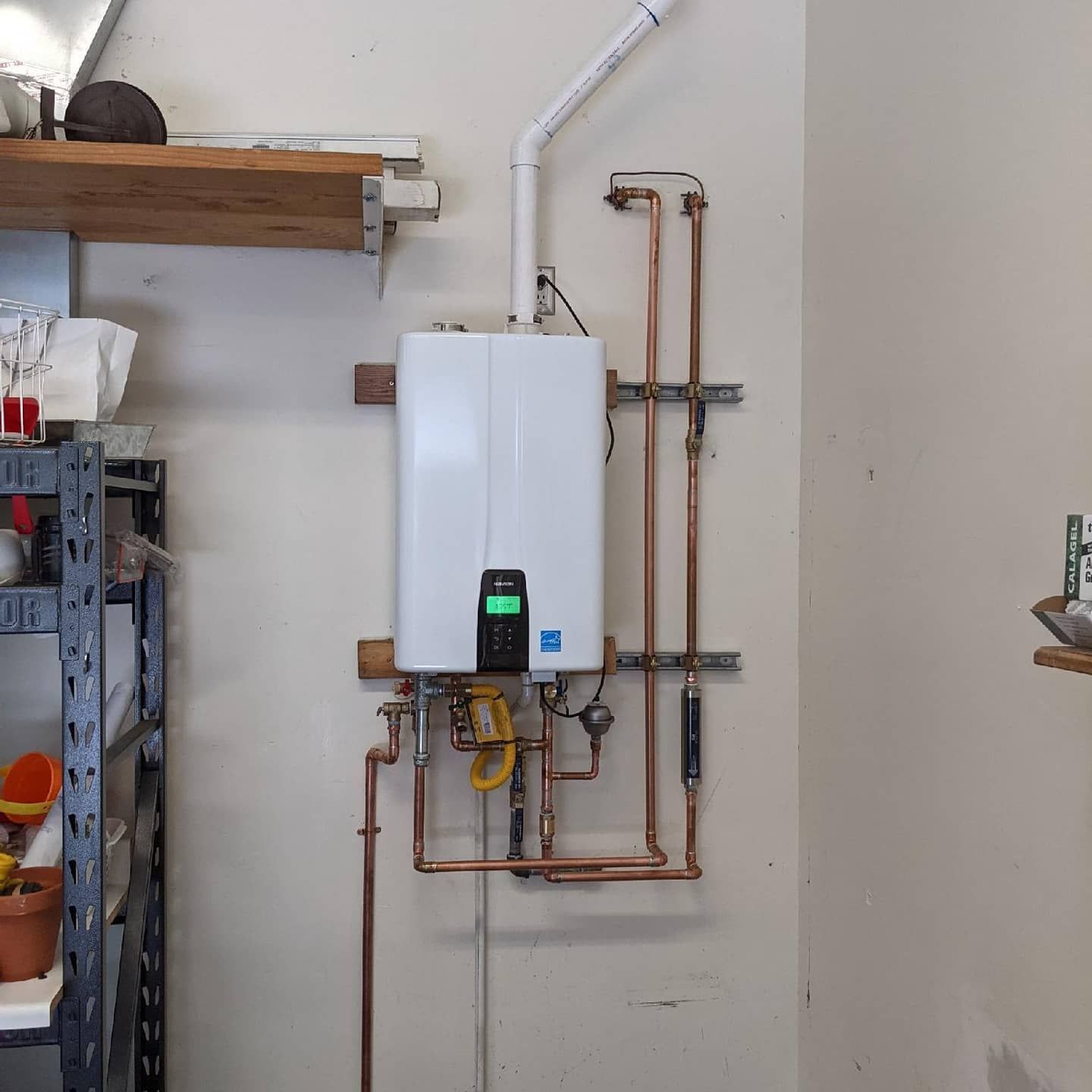 White tankless water heater mounted on a garage wall with copper pipes and ventilation.
