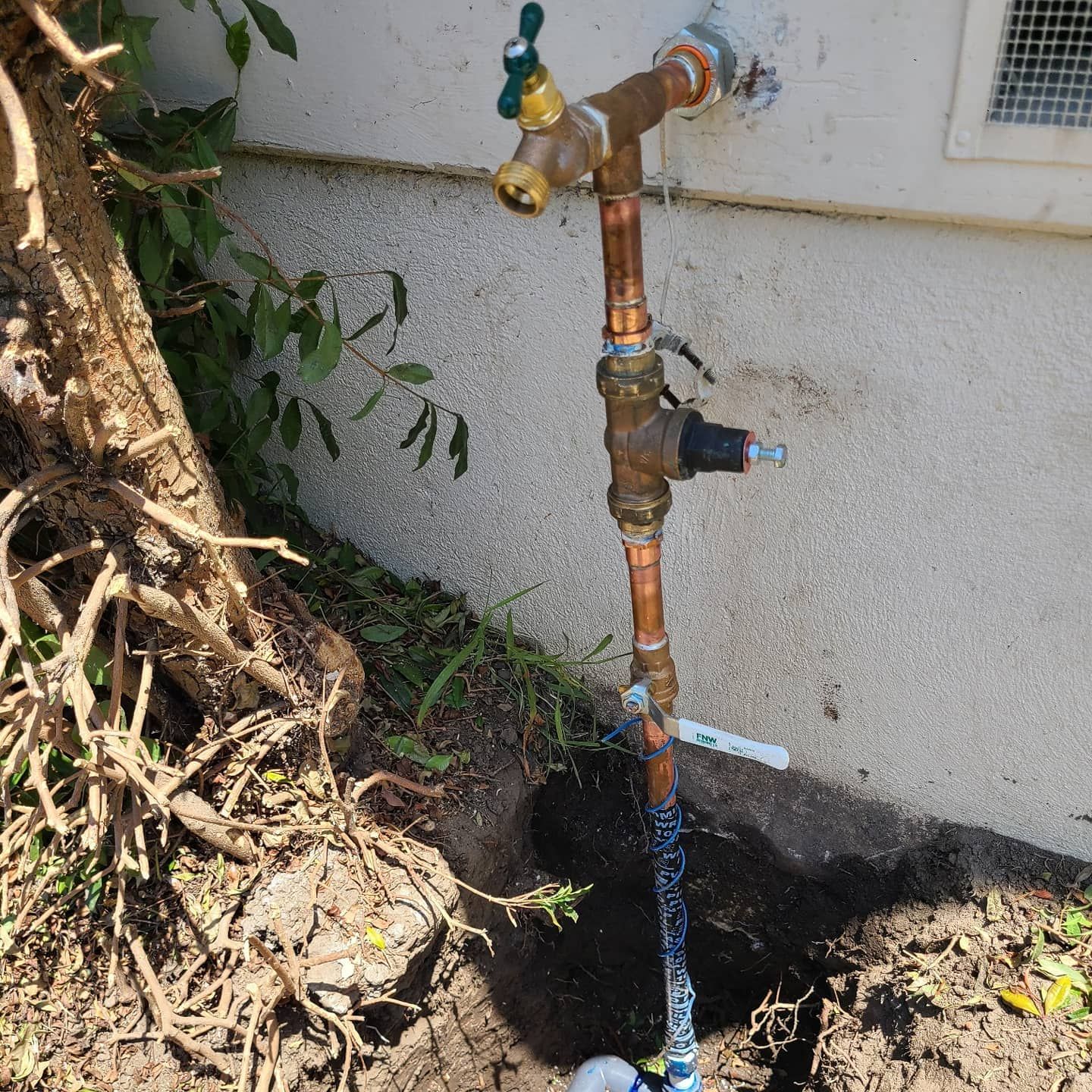 Copper plumbing connected to a spigot on a house exterior, with a small hole in the ground.