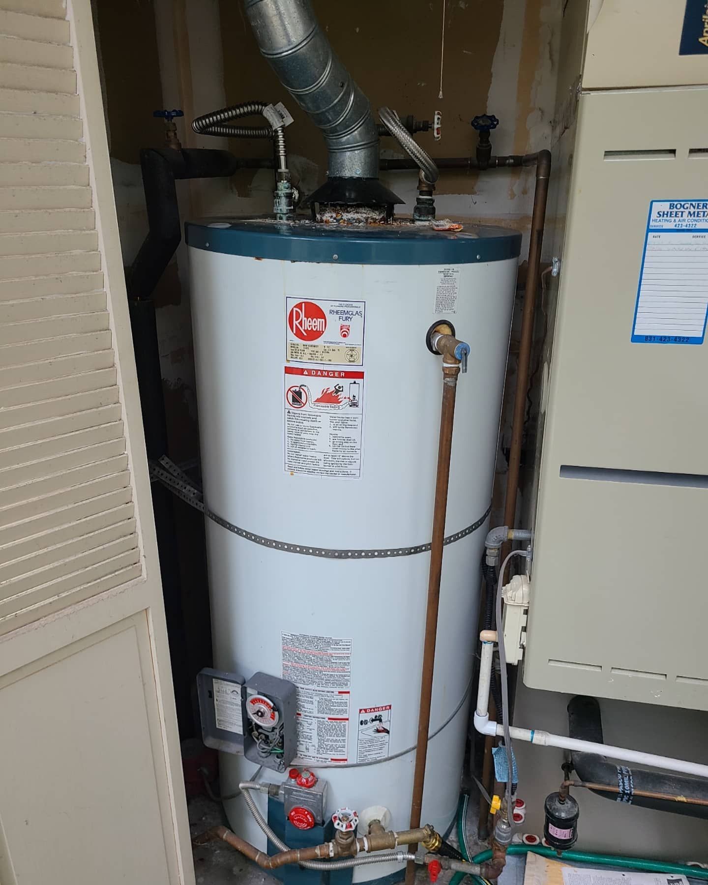 White water heater in a utility closet with a furnace to the right.